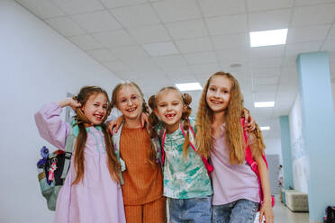 Happy schoolgirls standing with arm around in school corridor - MDOF01412