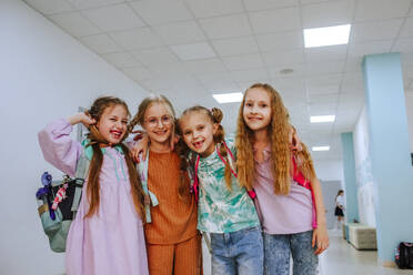 Cheerful schoolgirls standing with arm around in school corridor - MDOF01413