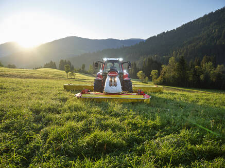 Landwirt mäht mit Traktor bei Sonnenaufgang ein Feld - CVF02441