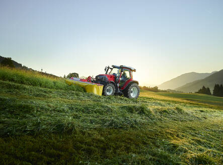 Landwirt mit Traktor und mäht Gras auf dem Land bei Sonnenaufgang - CVF02444