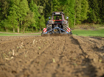 Landwirt ebnet den Boden mit einem Traktor auf einem Bauernhof bei Sonnenaufgang - CVF02449