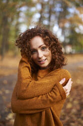 Smiling redhead woman wearing sweater at autumn park - ABIF02042