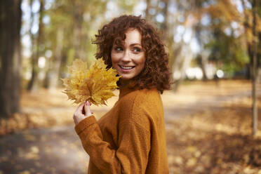 Beautiful redhead woman holding maple leaves at autumn park - ABIF02047