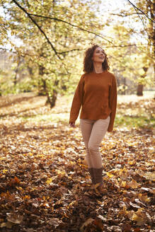 Rothaarige Frau steht auf Herbstblättern im Park - ABIF02055