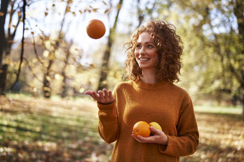 Lächelnde rothaarige Frau spielt mit Orangen und Zitronen im Herbst Park - ABIF02056