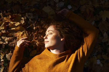 Redhead woman sleeping on autumn leaves at park - ABIF02078