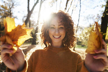 Happy redhead woman holding maple leaves at autumn park - ABIF02079