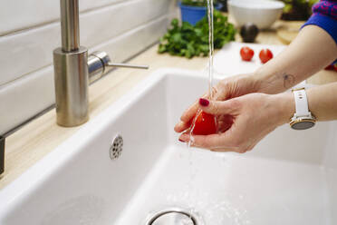 Hände einer Frau beim Waschen einer Tomate in der Spüle zu Hause - NJAF00414