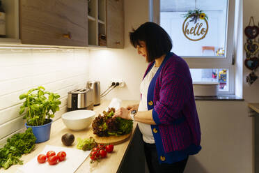 Schwangere Frau mit Gemüse bei der Zubereitung von Essen zu Hause - NJAF00415
