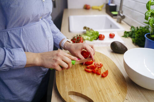 Pregnant woman cutting tomatoes with knife at home - NJAF00417
