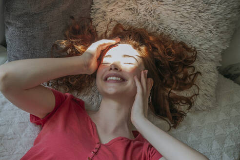 Glückliche Frau mit Sonnenlicht im Gesicht beim Entspannen zu Hause - OSF01750