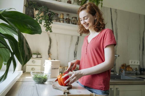 Glückliche junge Frau schneidet rote Paprika in der Küche zu Hause - OSF01755