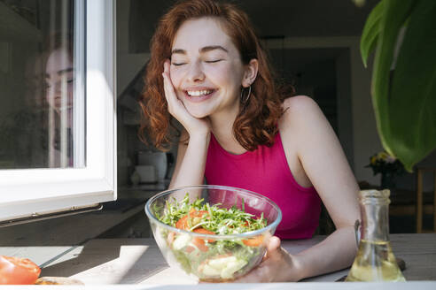 Glückliche Frau mit einer Schüssel Salat auf der Küchentheke lehnend - OSF01768