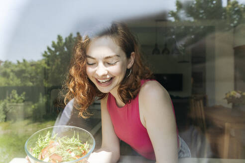 Glückliche junge Frau mit Salatschüssel durch Glas gesehen - OSF01769