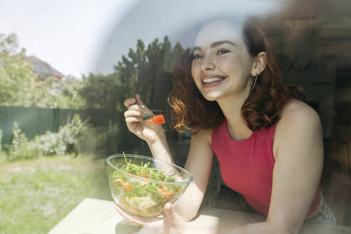 Glückliche junge Frau mit Salatschüssel durch Glas gesehen - OSF01770