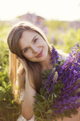 Smiling woman holding bunch of purple lupine flowers - ONAF00561