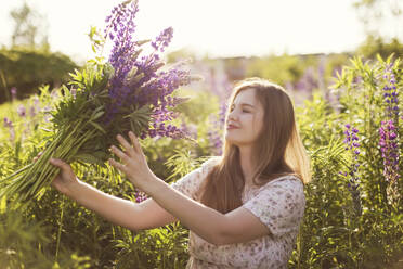 Happy woman holding bunch of lupine flowers in field - ONAF00562