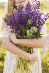 Woman standing with purple lupine flowers - ONAF00567