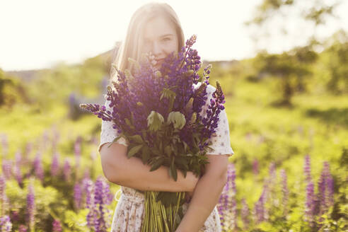 Lächelnde Frau mit lila Lupinenblüten auf einem Feld an einem sonnigen Tag - ONAF00568