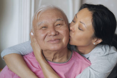 Erwachsene Tochter küsst älteren Vater zu Hause auf die Wange - AZF00539