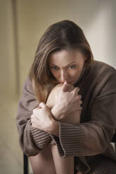 Worried woman hugging knee sitting at home - AZF00541