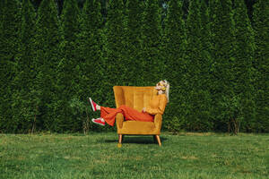 Blonde Frau sitzt auf einem Sessel im Garten - VSNF01094