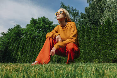 Woman wearing sunglasses crouching in garden - VSNF01104