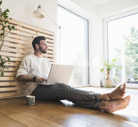 Thoughtful businessman sitting with laptop at home - UUF29044