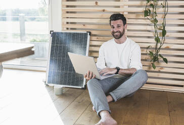 Glücklicher Geschäftsmann mit Laptop vor einem Sonnenkollektor zu Hause - UUF29053