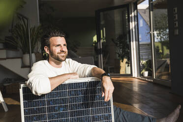 Lächelnder Freiberufler, der mit einem Solarpanel zu Hause sitzt - UUF29057