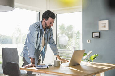 Businessman working on laptop in home office - UUF29069