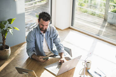 Businessman using mobile phone at desk in home office - UUF29089