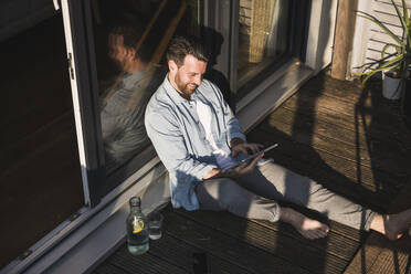 Glücklicher Freiberufler mit Tablet-PC auf der Veranda - UUF29112