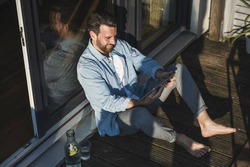 Happy freelancer using tablet PC on porch at home - UUF29113