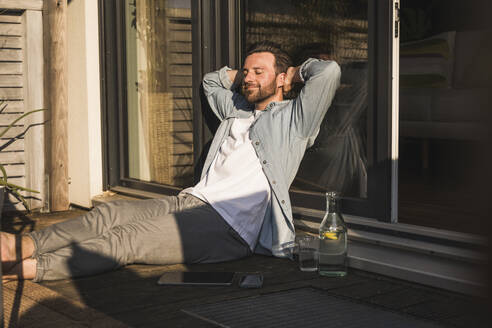 Smiling freelancer with hands behind head sitting on porch - UUF29116