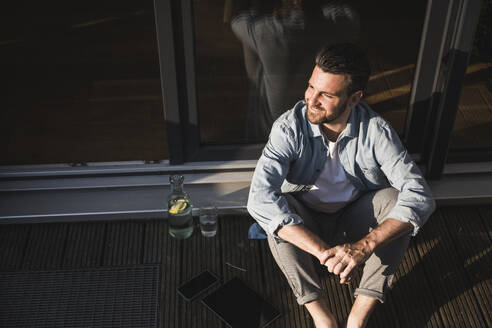 Happy freelancer with hands clasped sitting on porch - UUF29119