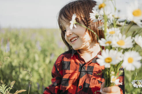 Lächelnder Junge mit Blumenstrauß auf einem Feld - ANAF01556