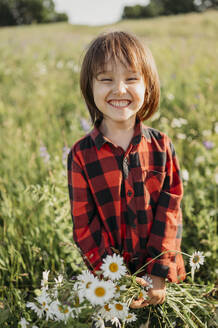 Junge mit zahnigem Lächeln hält Blumenstrauß im Feld - ANAF01559