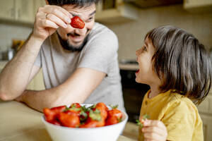 Father feeding strawberry to son from bowl - ANAF01568