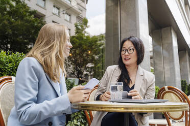 Businesswoman discussing with partner sitting at table in sidewalk cafe - NDEF00821