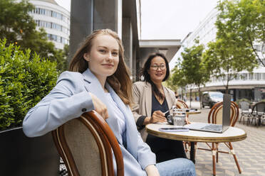 Lächelnde Geschäftspartner sitzen am Tisch in einem Straßencafé - NDEF00822