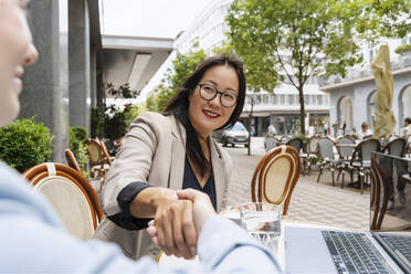 Geschäftspartner beim Händeschütteln am Tisch in einem Straßencafé - NDEF00823