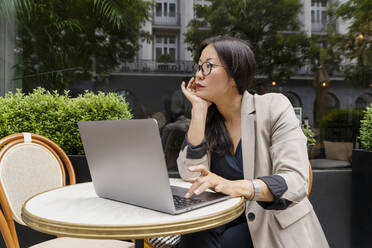 Geschäftsfrau arbeitet mit Laptop auf einem Tisch in einem Straßencafé - NDEF00825