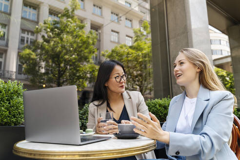 Businesswoman discussing with partner at sidewalk cafe - NDEF00833