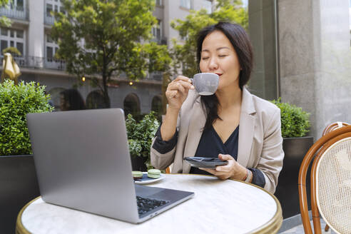 Geschäftsfrau genießt Kaffee mit Laptop auf einem Tisch in einem Straßencafé - NDEF00838