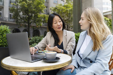 Business partners discussing with laptop and coffee on table at sidewalk cafe - NDEF00840