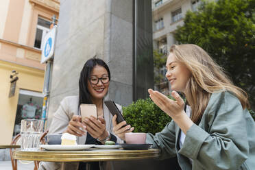 Smiling business partners using smart phones sitting at sidewalk cafe - NDEF00844