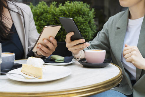 Geschäftspartner mit Smartphones bei Kaffee und Kuchen auf einem Tisch in einem Straßencafé - NDEF00845