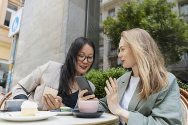 Geschäftspartner, die mit Smartphones in einem Straßencafé diskutieren - NDEF00846