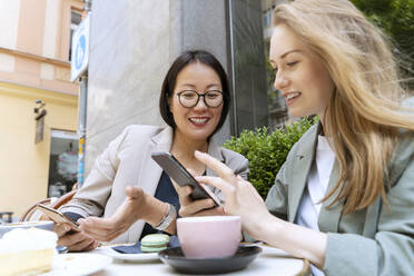 Glückliche Geschäftspartner, die in einem Straßencafé mit ihren Smartphones diskutieren - NDEF00848